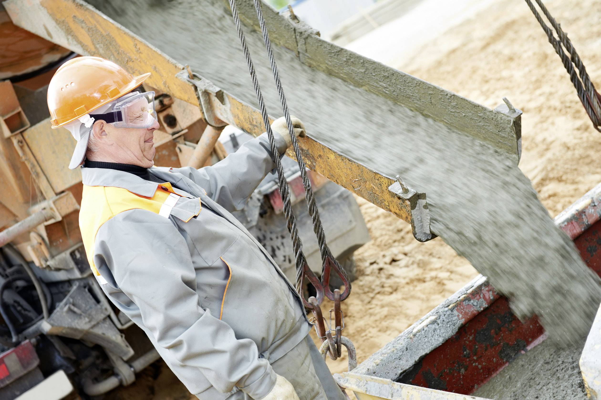 Ein Bauarbeiter in Schutzkleidung lenkt fließenden Beton von einem Lastwagen in eine Bodenschalung auf einer Baustelle.