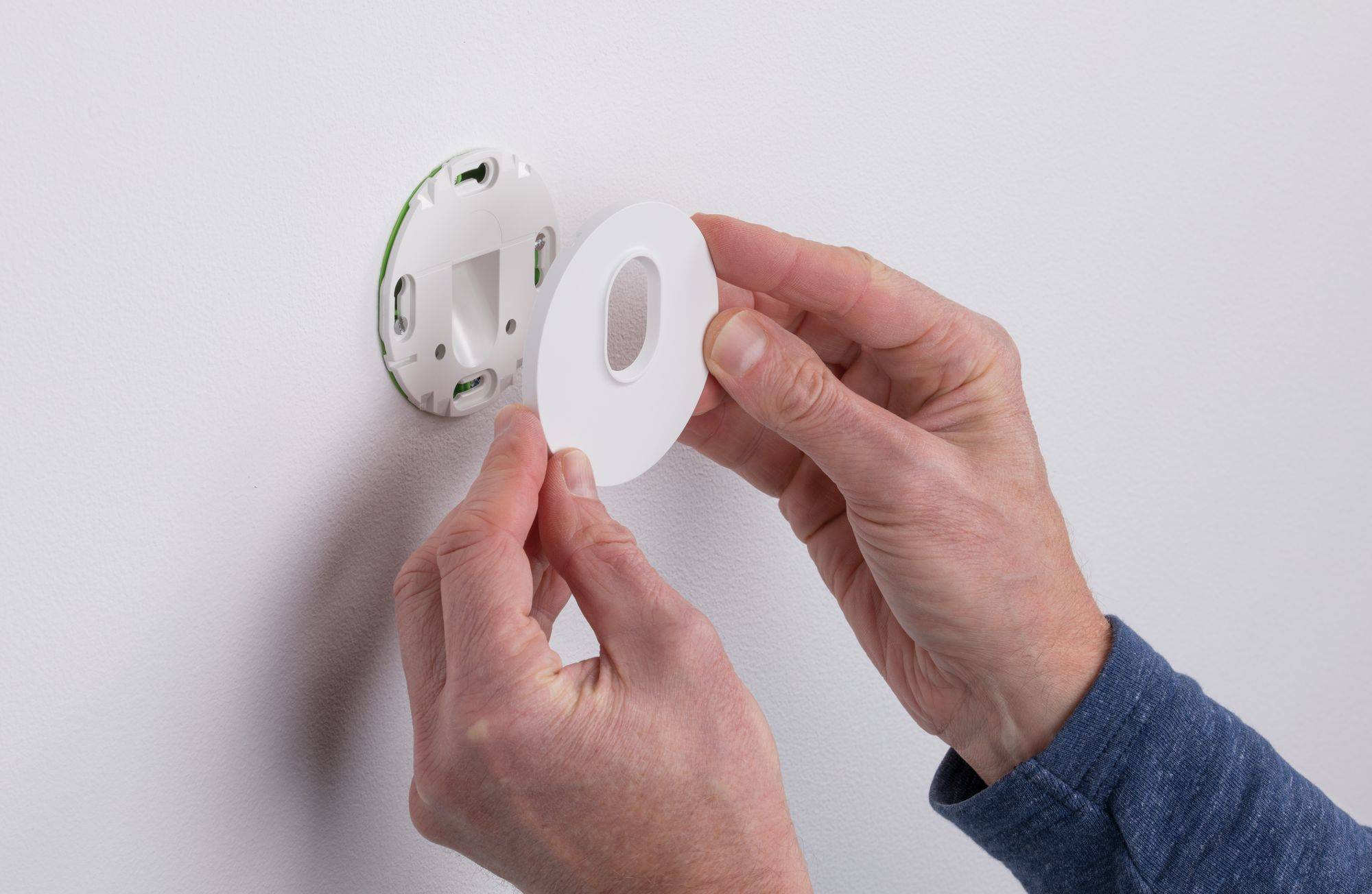 Eine Person installiert eine runde, weiße Abdeckplatte auf einem Wandstecker oder Schalter, wobei sie die Platte in der Hand hält.