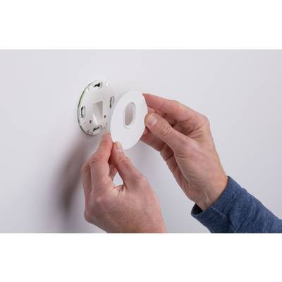 Person befestigt eine runde Abdeckung an einer Wandhalterung, möglicherweise für ein Thermostat oder ein ähnliches Gerät.