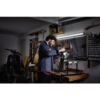 Ein Mann arbeitet in einer voll ausgestatteten Werkstatt an einem Metallprojekt. Er benutzt eine Maschine, um das Werkstück zu bearbeiten.