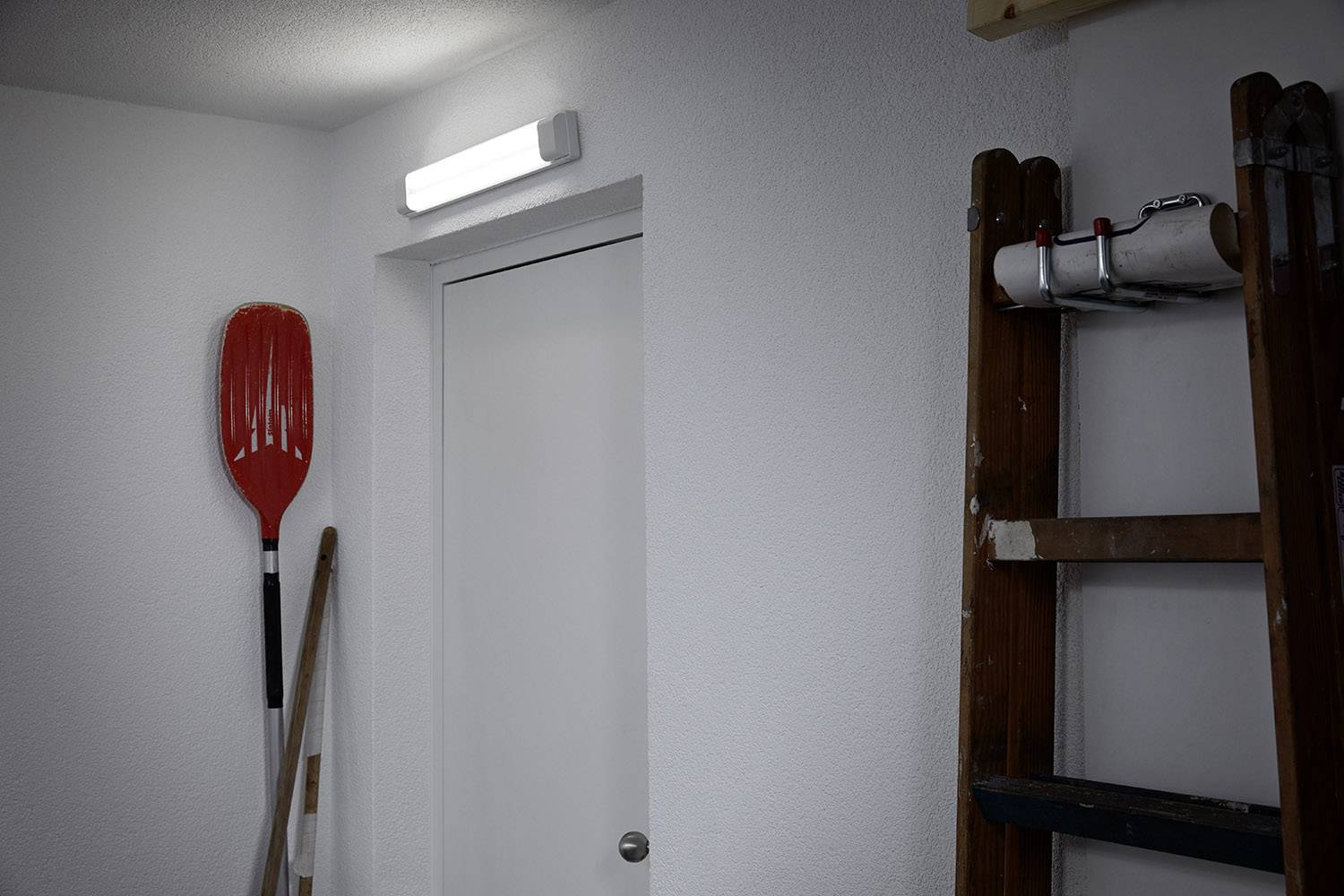 Ein heller Raum mit geschlossenen weißen Türen. An der Wand hängt ein rotes Paddel. Rechts davon lehnt eine Holzleiter.
