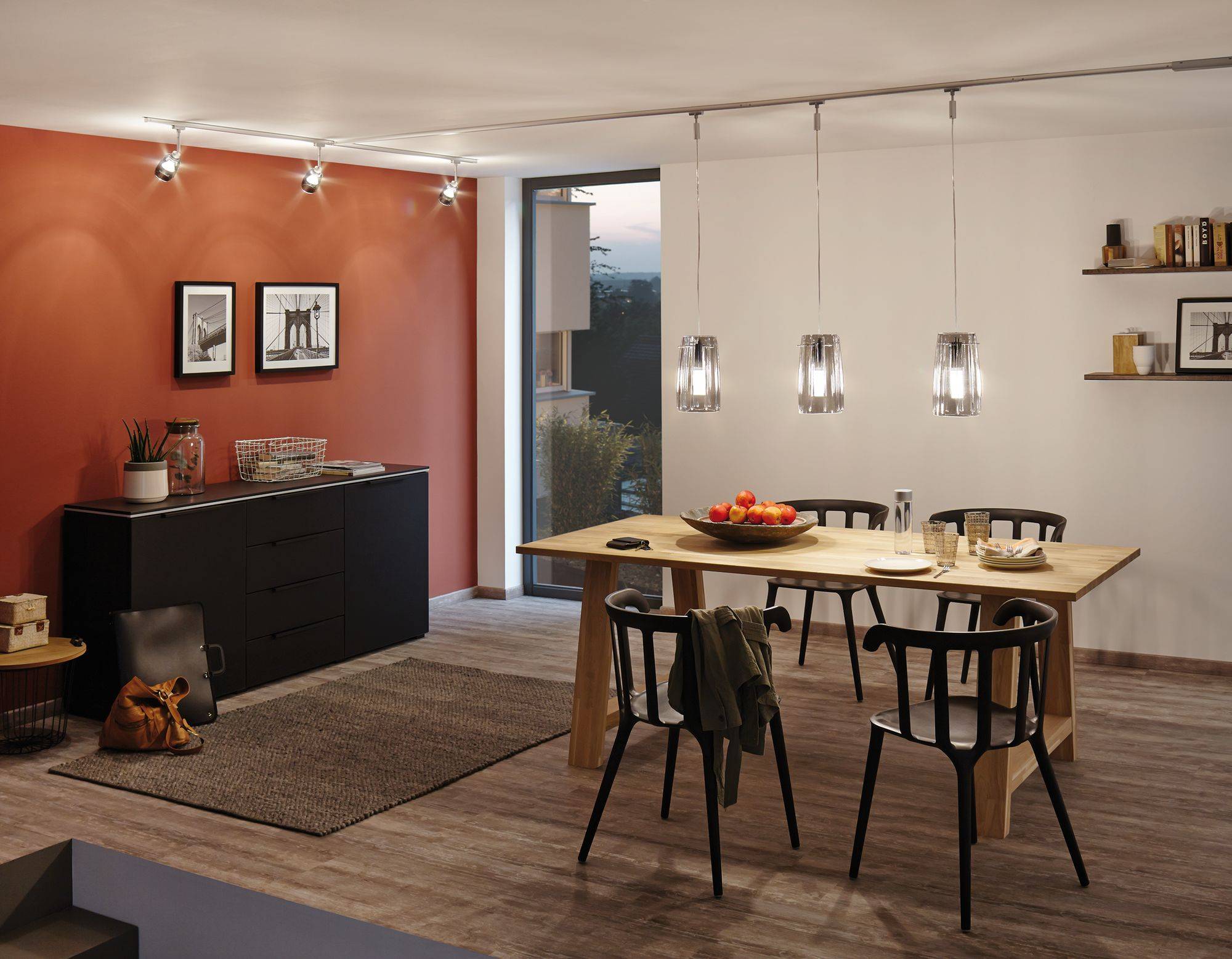 Esszimmer mit Holztisch, Stühlen und modernen Lampen. Rote und weiße Wände. Fenster mit Aussicht. Dekorative Bilder und Regal.