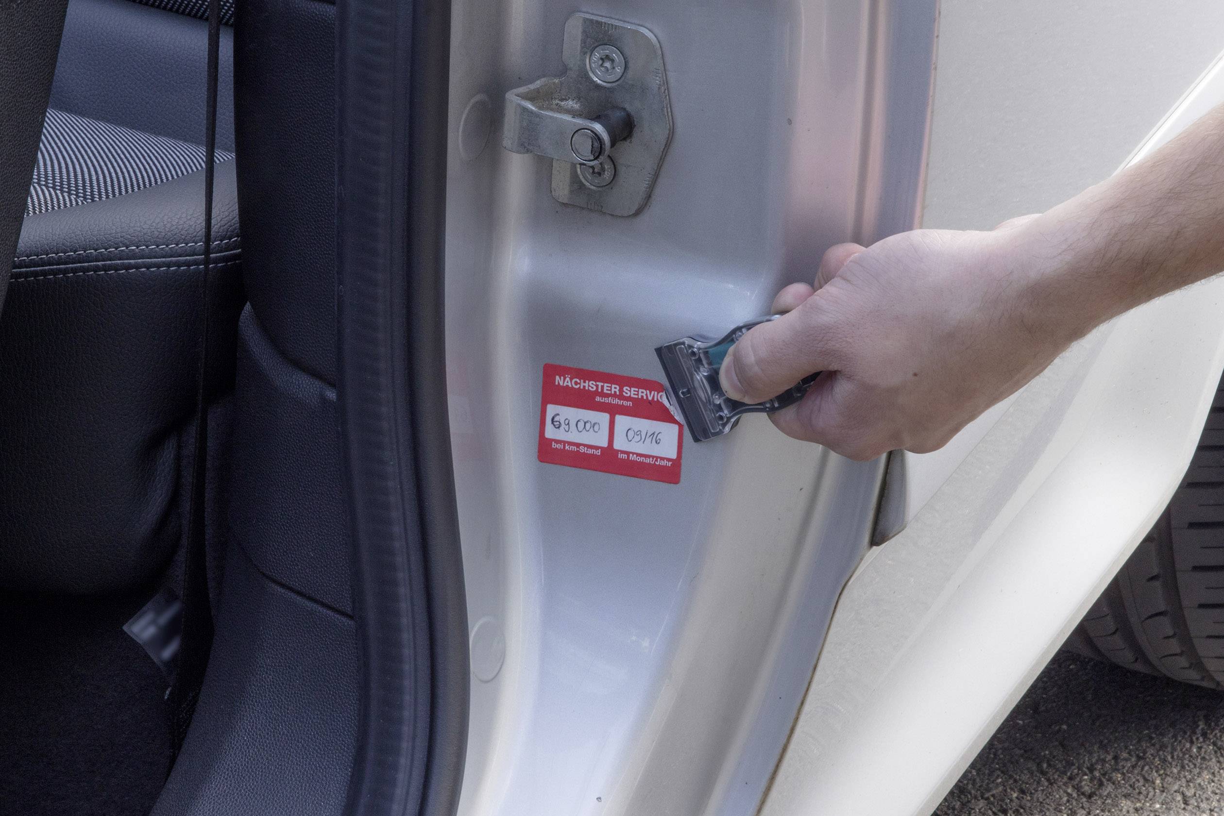 Eine Hand zeigt auf einen Aufkleber am Türrahmen eines Autos, der Informationen über Fahrzeugemissionen enthält.