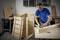 Ein Mann in blauer Poloshirt montiert eine Holzbox in einer Werkstatt. Werkzeug und weitere Holzplatten sind im Hintergrund zu sehen.