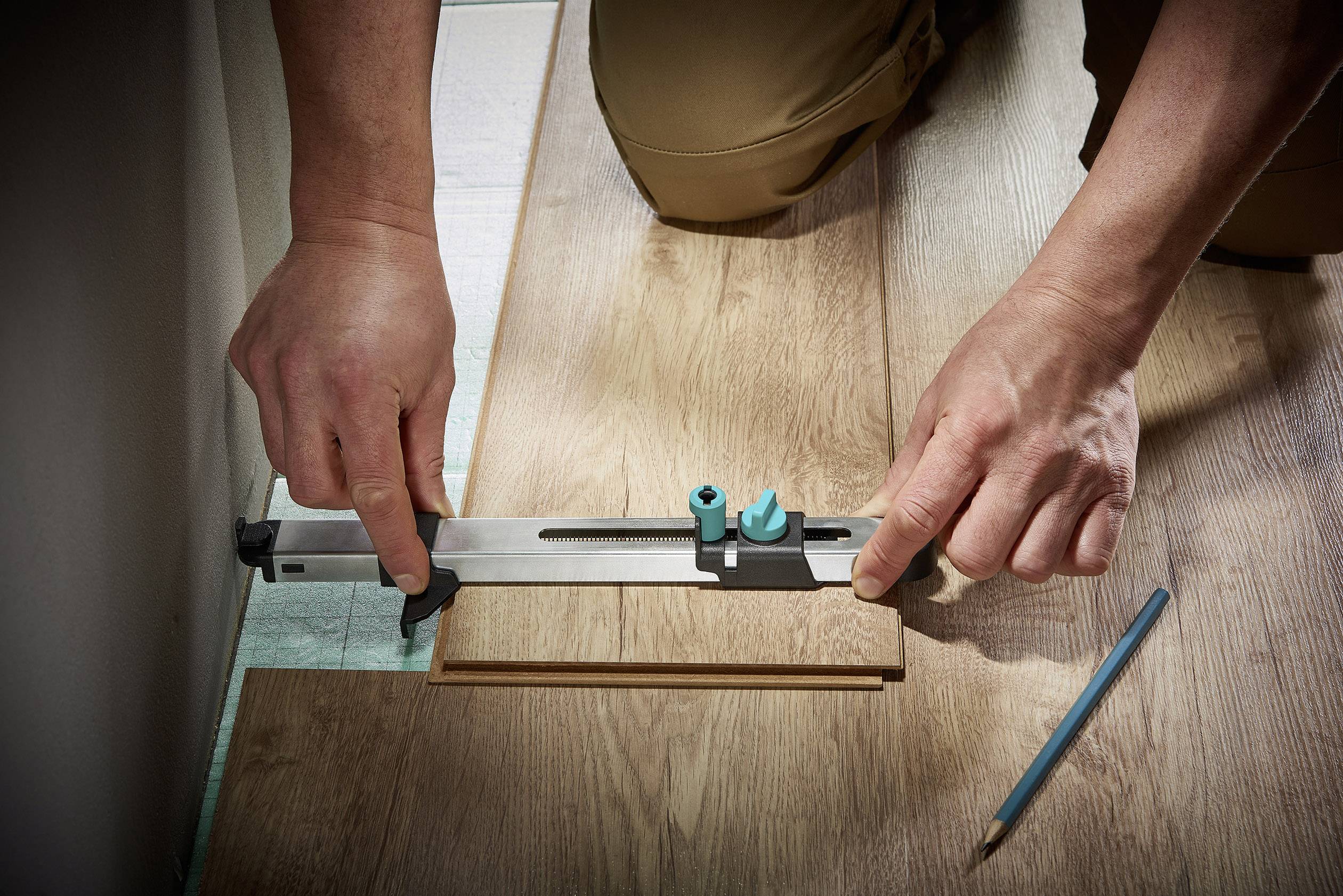 Eine Person misst ein Holzbrett mit einem Winkelmesser zum präzisen Zuschneiden, ein Bleistift liegt daneben auf dem Boden.
