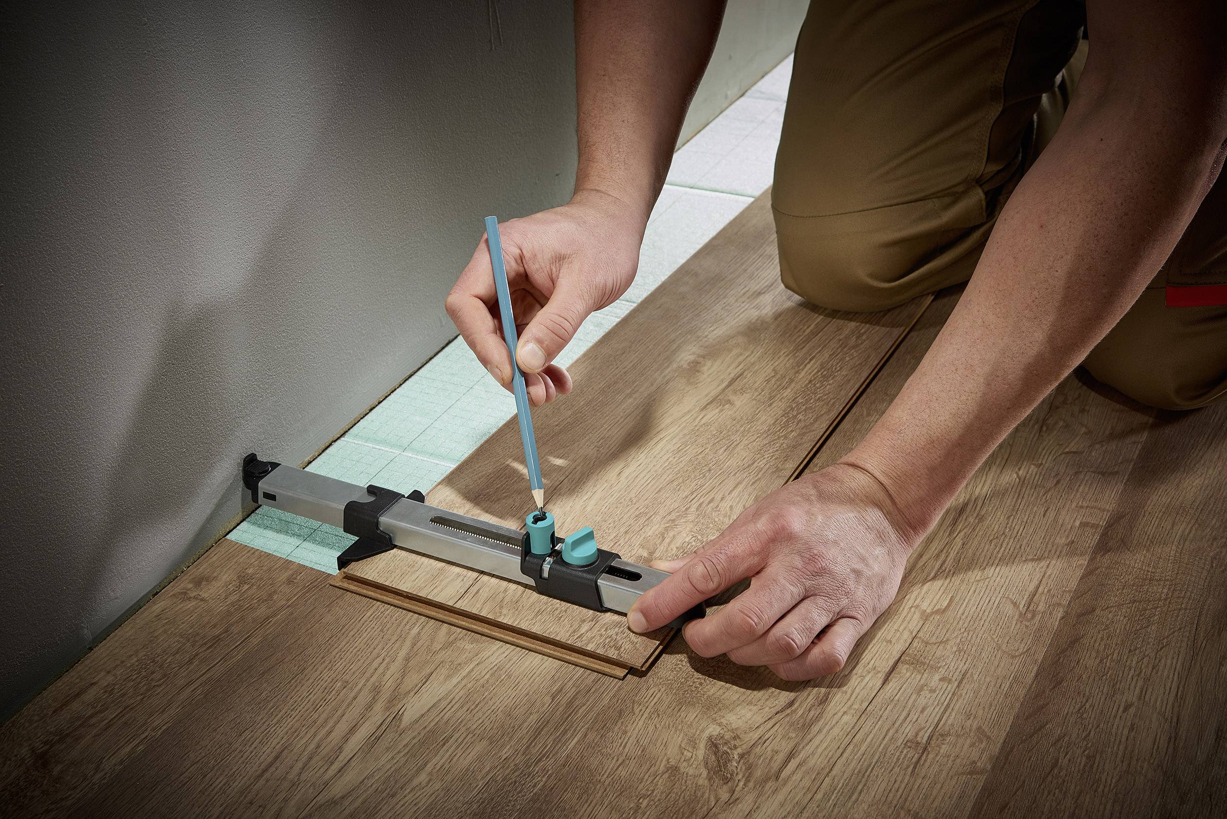 Eine Person misst mit einem Werkzeug die Breite einer Lücke zur Wand, um Laminatboden passgenau zuzuschneiden.