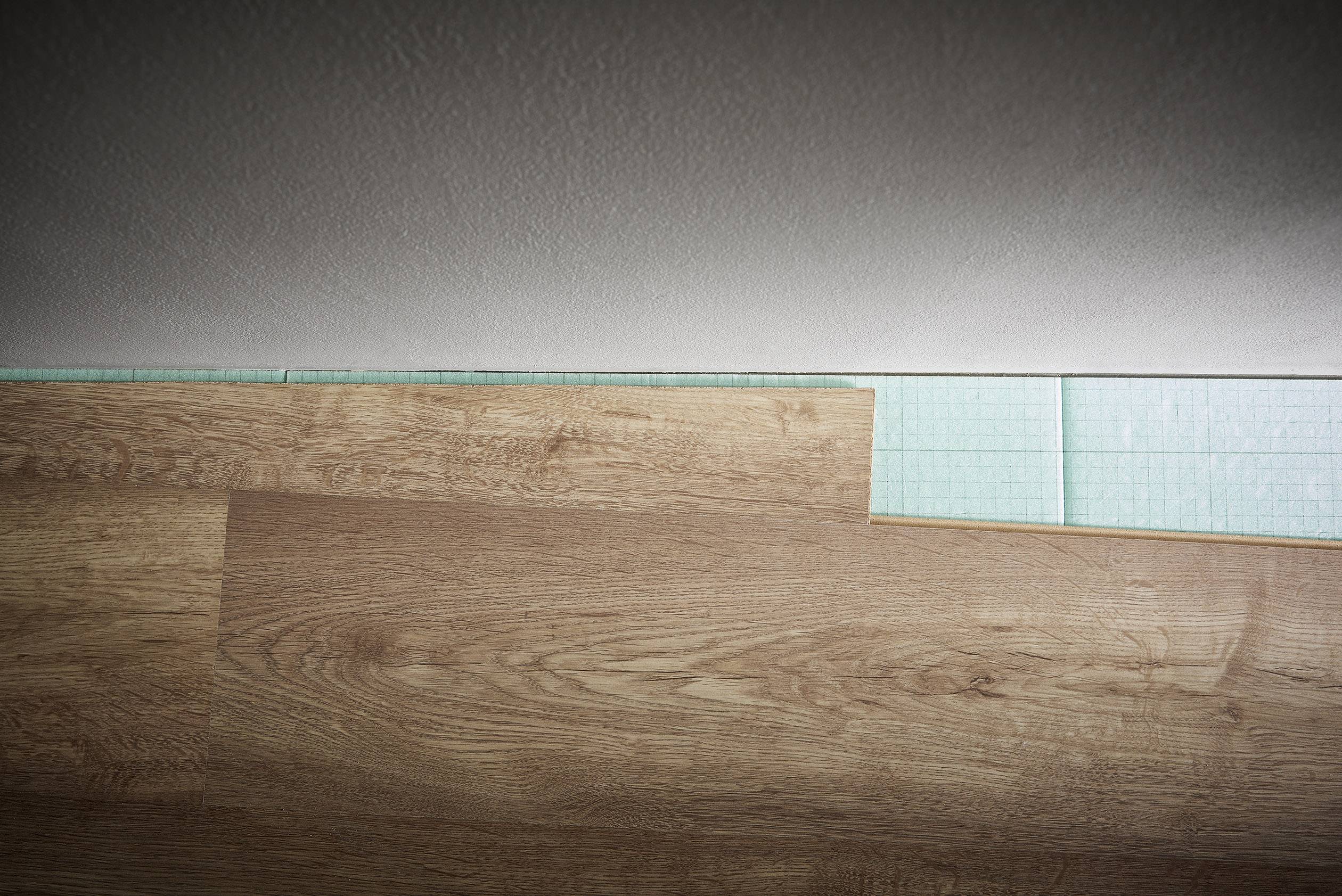 Eine Laminatdiele wird mit einer grünen Trittschalldämmung verlegt. Diele passt teilweise in die bestehende Lücke an der Wand.