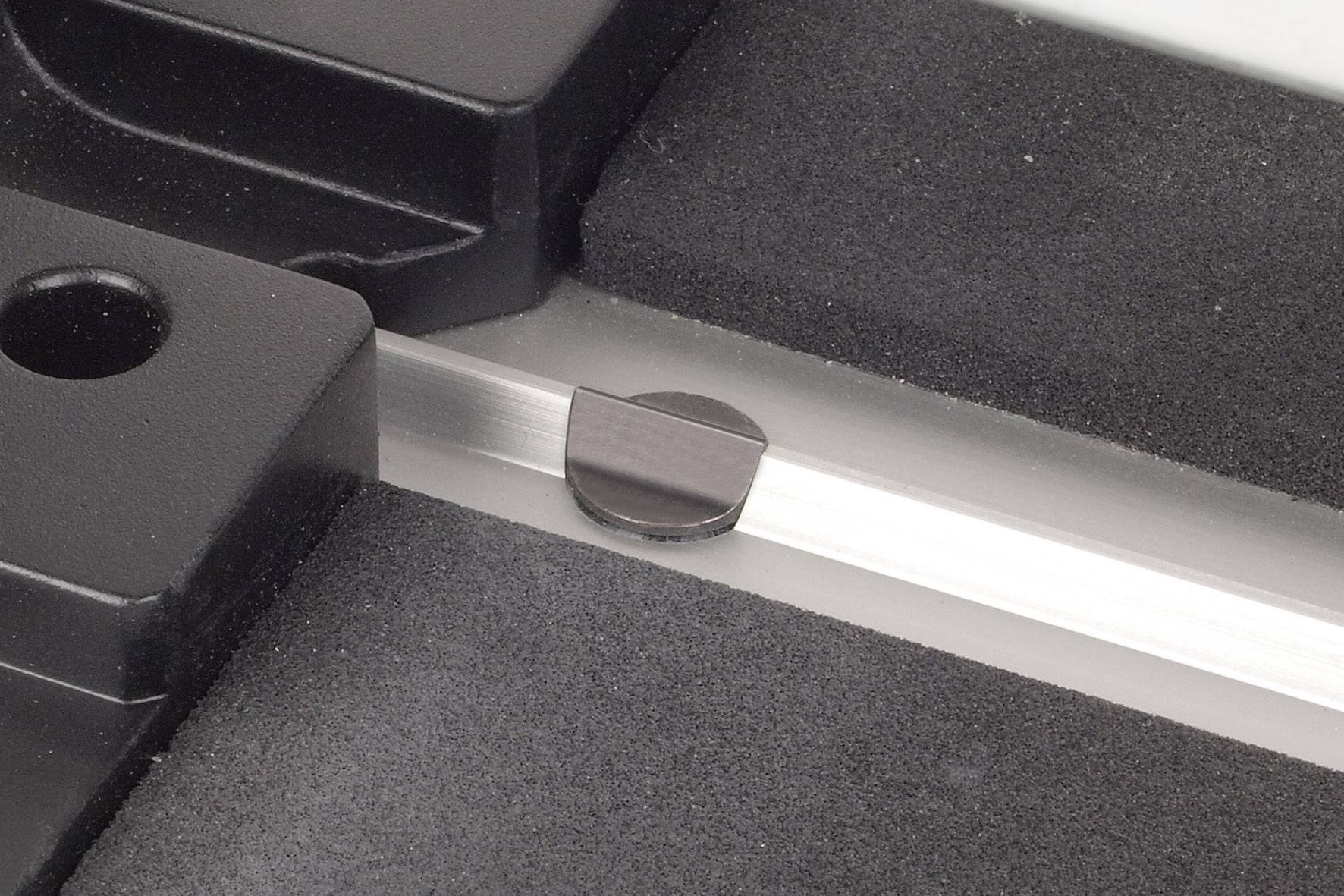 Eine runde, schwarze Kunststoffscheibe sitzt fest in einer klaren, metallischen Führungsschiene. Daneben liegen schwarze Gummipuffer.