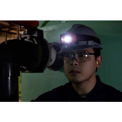 Ein Mann trägt einen Helm mit Stirnlampe und Schutzbrille, arbeitet in einer industriellen Umgebung.