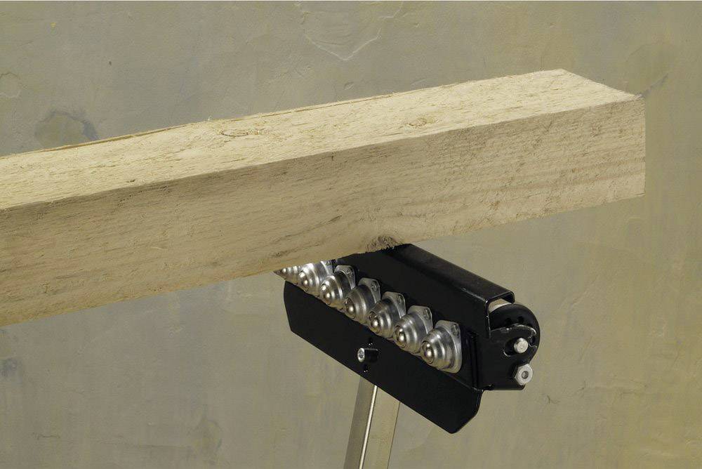 Ein Holzbalken liegt auf einer Metallvorrichtung mit Rollenlagern auf einem Stativ, möglicherweise zur Unterstützung beim Schneiden.
