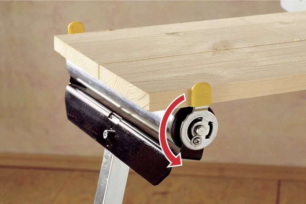 Ein Holztisch wird durch eine Klemmvorrichtung und ein Zahnrad befestigt. Ein roter Pfeil zeigt die Drehrichtung des Zahnrads an.