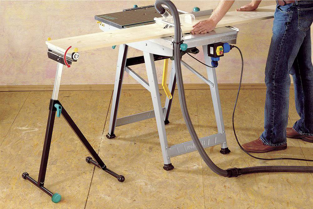 Eine Person sägt mit einer Tischkreissäge ein Holzbrett, unterstützt von einem Rollständer.