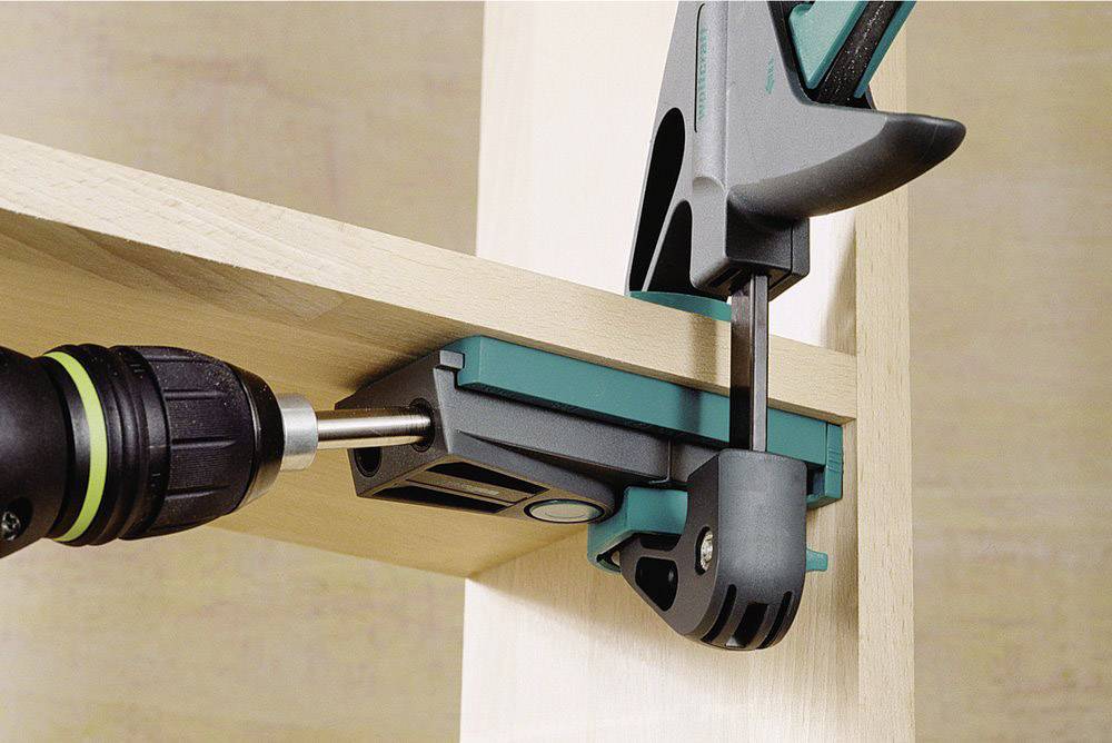 Ein Bohrer befestigt ein Brett an einem vertikalen Balken mit einer Klemme. Die Klemme sorgt für Stabilität während der Arbeit.