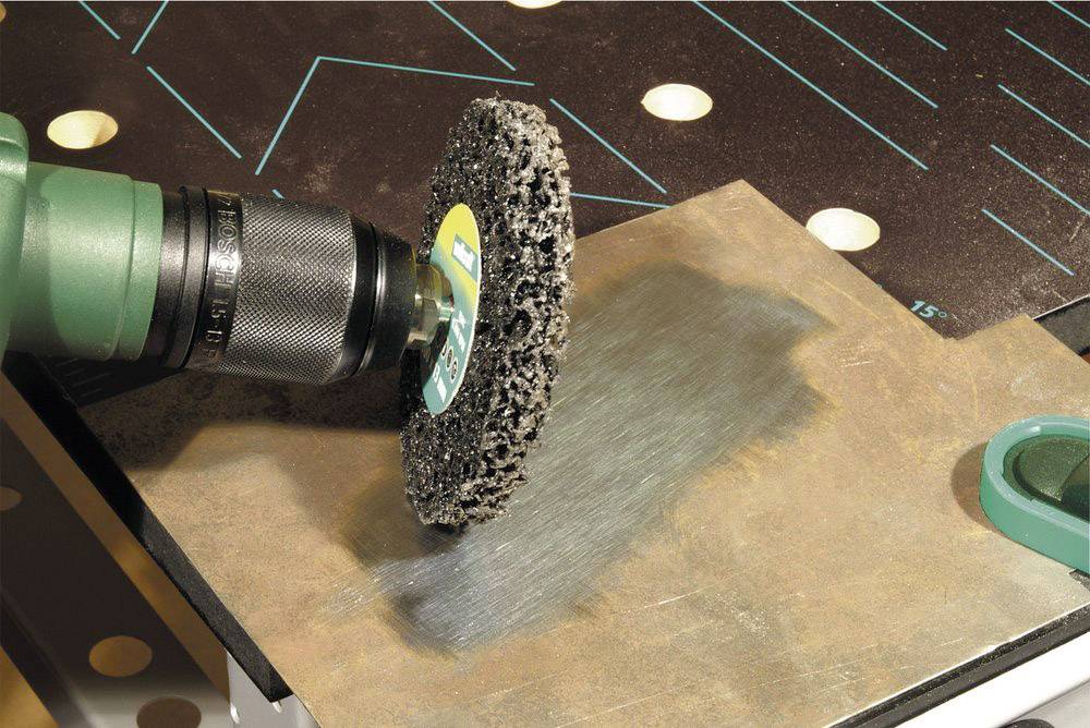 Eine Schleifmaschine glättet die Oberfläche eines Metallblechs. Sie erzeugt eine sichtbare polierte Fläche auf dem Material.