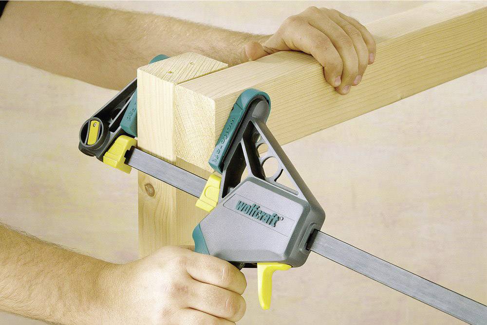 Eine Person verwendet eine Einhandzwinge, um zwei Holzbalken rechtwinklig zu fixieren. 