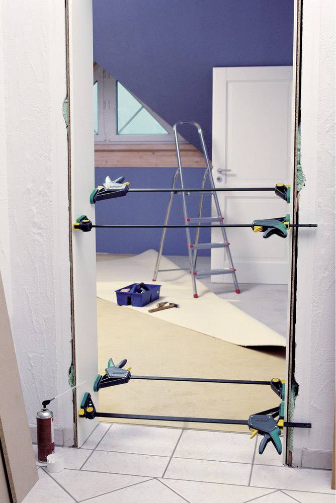 Türrahmen wird mit Zwingen eingesetzt; im Hintergrund Leiter und Werkzeugkasten, Renovierungsarbeiten im Gange.