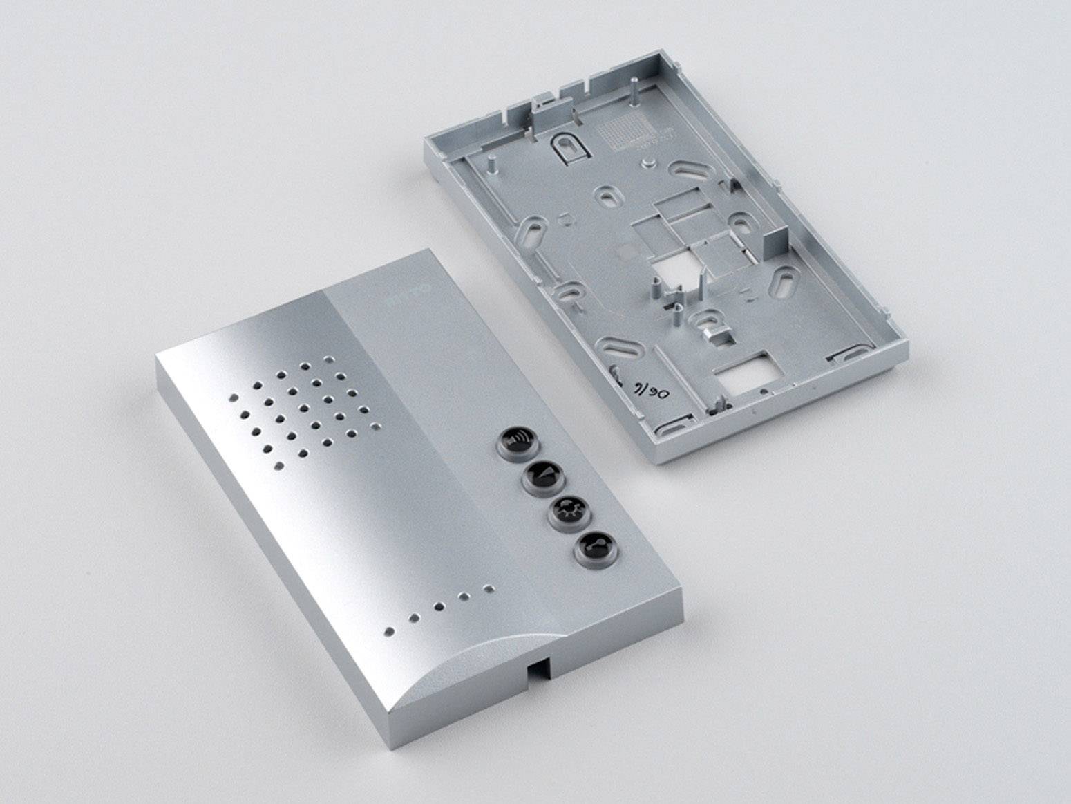 Ein zerlegtes Gehäuse eines elektronischen Geräts, bestehend aus einer Abdeckung mit Lüftungsschlitzen und drei Tasten, neben einer Rückplatte.