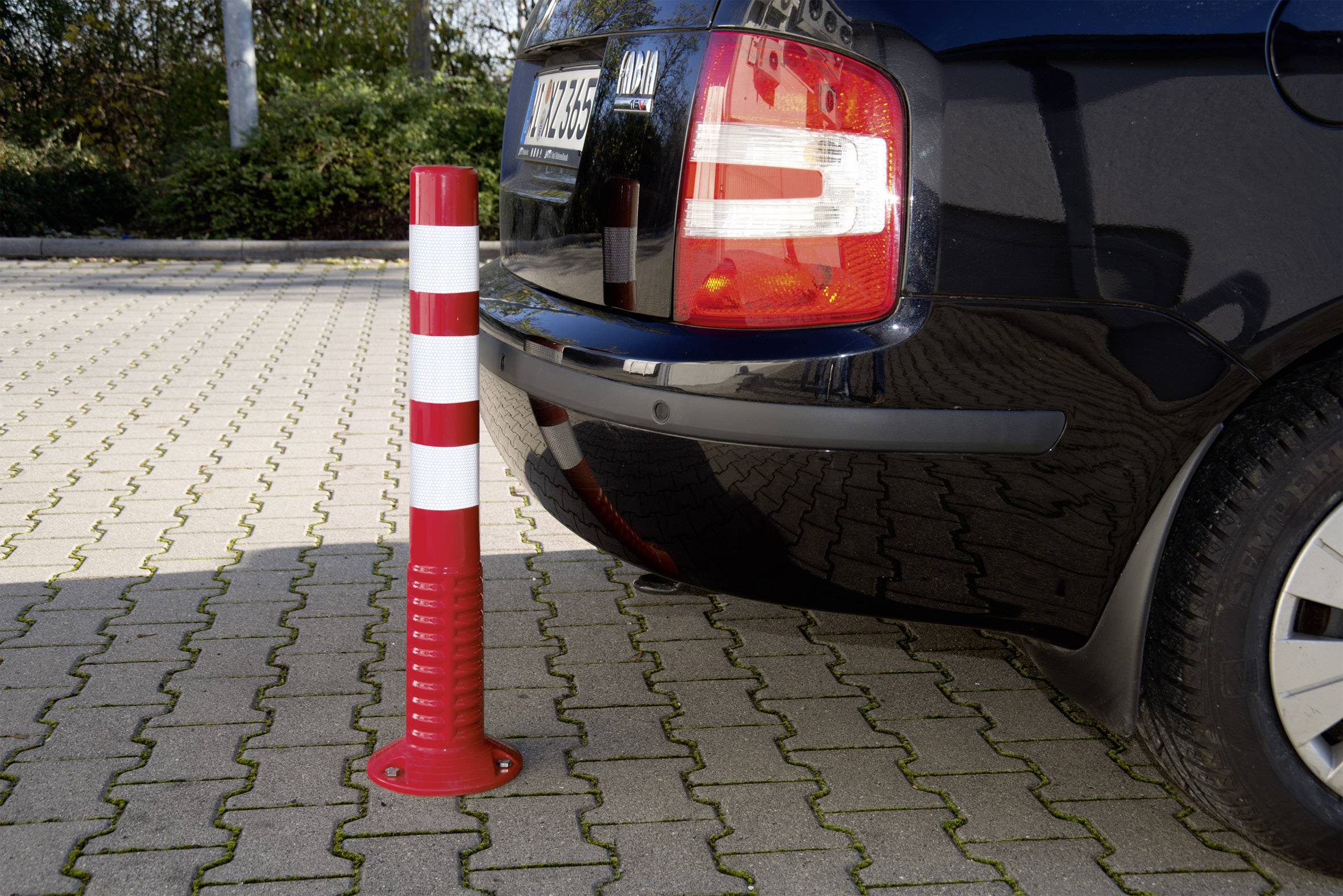 Ein rot-weißer Poller steht dicht vor dem Heck eines schwarzen Autos auf einem gepflasterten Parkplatz.