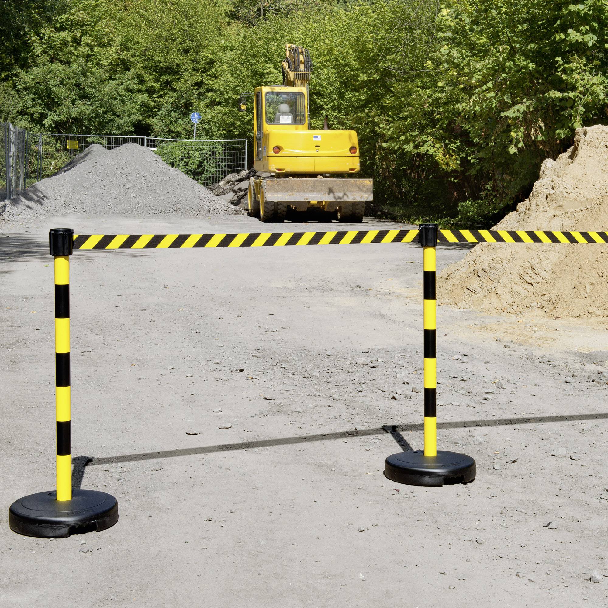 Bauarbeiten mit gelbem Bagger und Erdhaufen auf einer Baustelle, abgesperrt durch gelb-schwarz gestreifte Sicherheitsbarrieren.