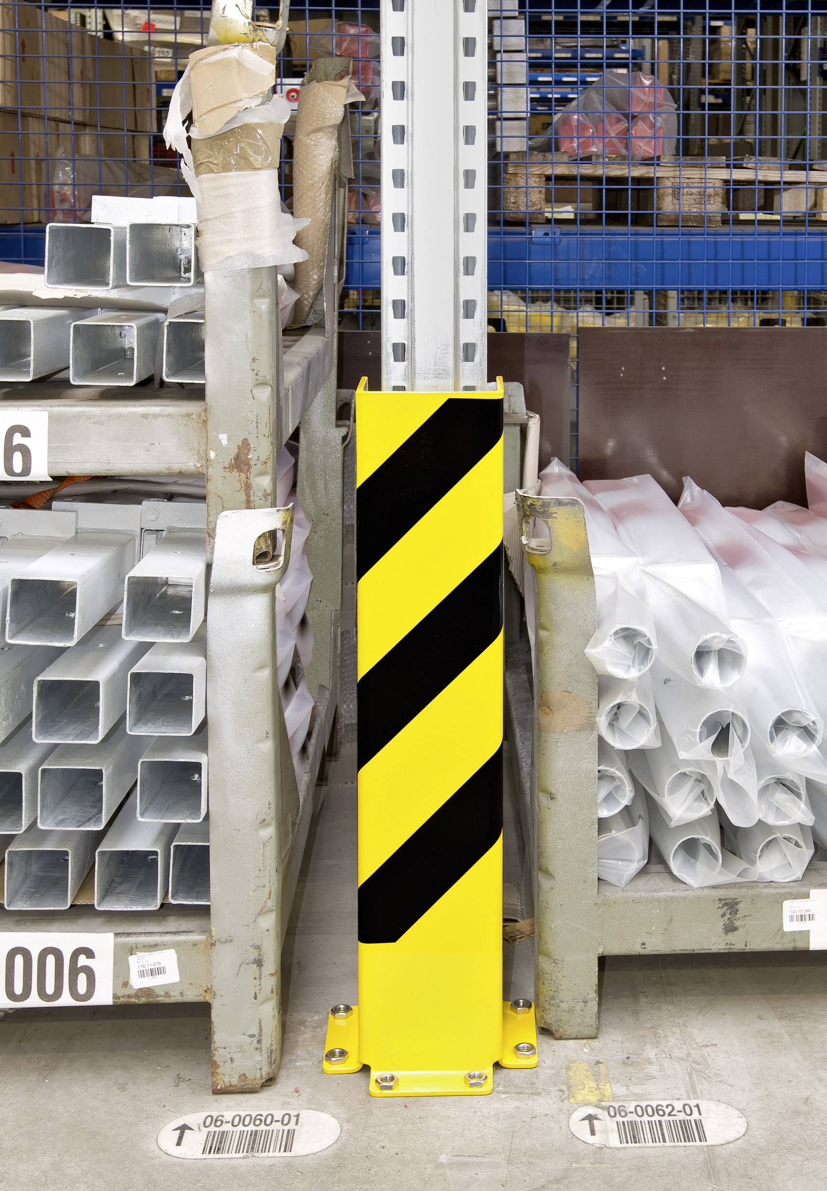 Gelber Schutzpfosten mit schwarzen Streifen schützt eine Metallstütze in einem Lager. Stapel von Metallrohren sind rechts und links sichtbar.