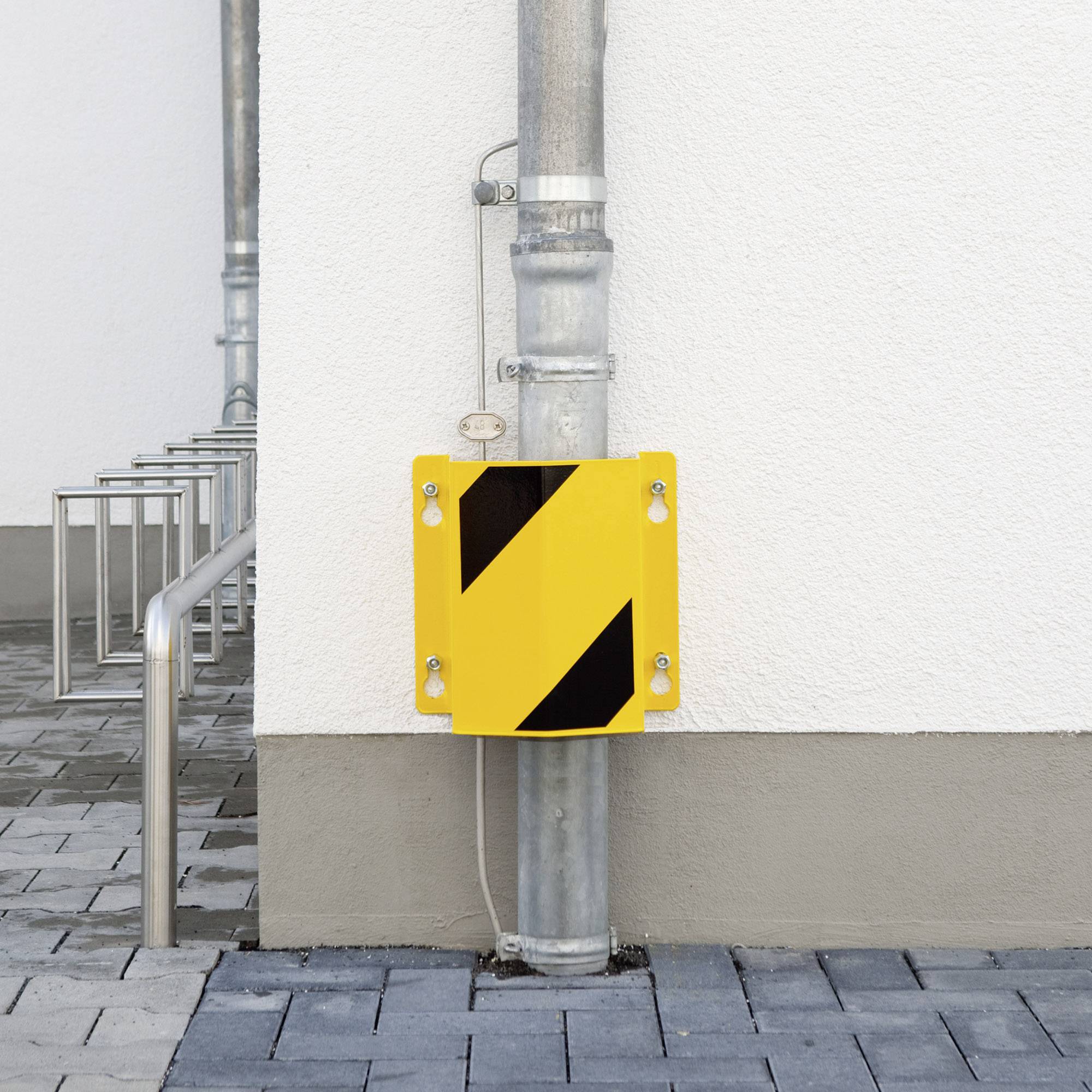 Eine gelbe Schutzvorrichtung mit schwarzen Streifen ist an einem Rohr neben einem Gehweg angebracht.