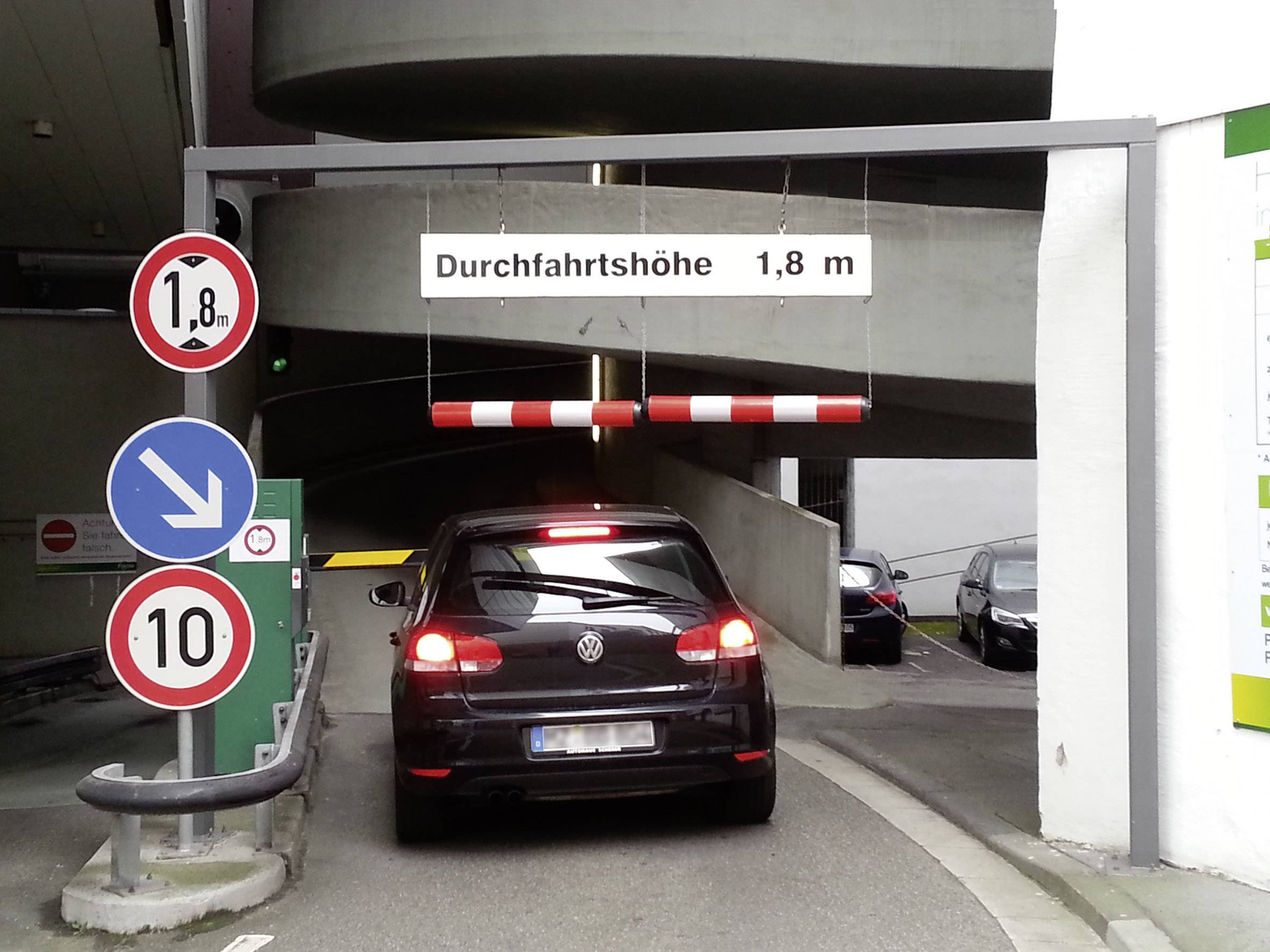 Auto im Parkhaus-Eingang. Schilder zeigen 'Durchfahrthöhe 1,8 m', Geschwindigkeitsbegrenzung 10 km/h und Einfahrtsregelungen.