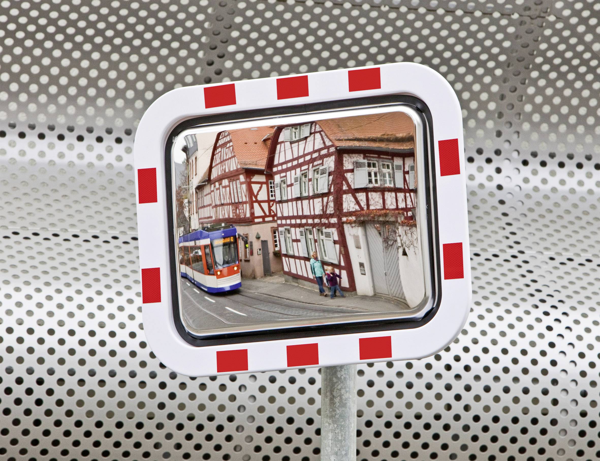 Ein Sicherheitsspiegel zeigt eine Straßenbahn und Fachwerkhäuser in einer Stadt. Reflektiert ist eine Straßenszene mit Fußgängern.