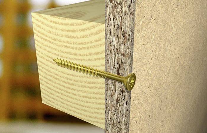 Eine goldene Schraube verbindet ein Holzbrett mit einer Spanplatte.
