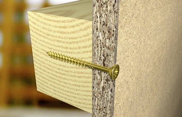 Eine goldene Schraube verbindet ein Holzbrett mit einer Spanplatte. Die Schraube ist mittig im Brett platziert und vollständig eingedreht.