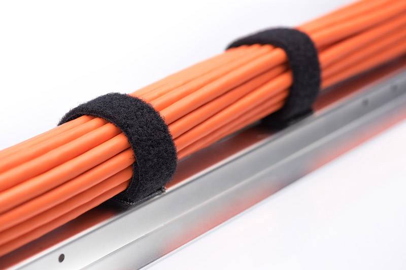 Rote Kabel, gebündelt mit schwarzen Klettbändern, auf einem silbernen Kabelkanal.