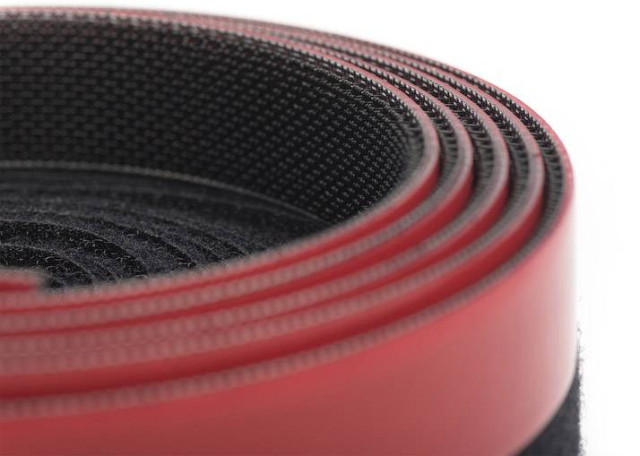 Ein aufgerolltes Stück schwarzes Klettband mit einer roten Umrandung, das eng gewickelt ist und eine spiralförmige Anordnung zeigt.