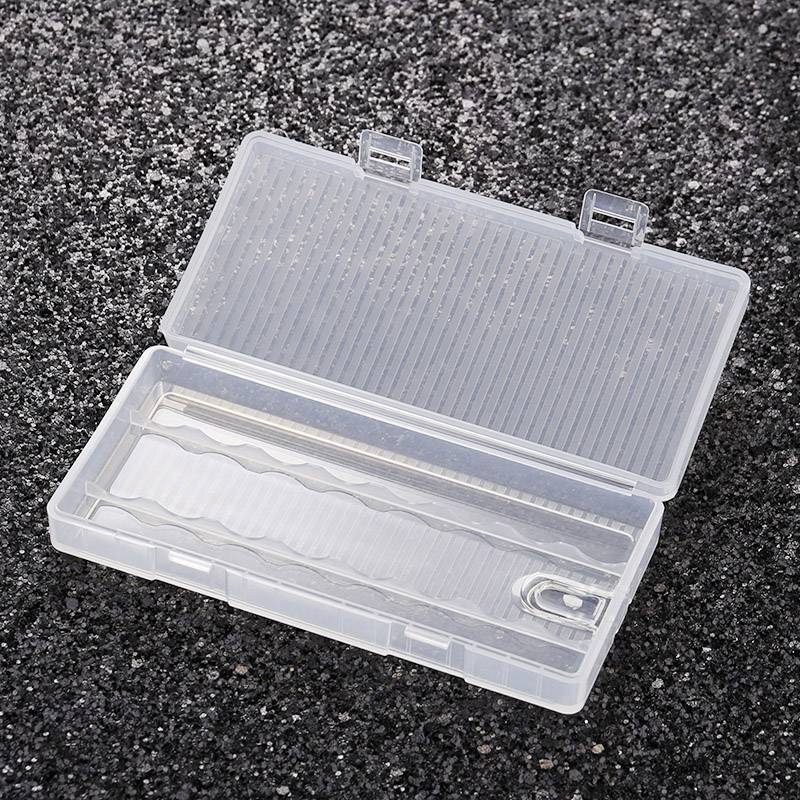 Ein transparenter Kunststoffbehälter mit Fächern liegt offen auf einer dunklen, asphaltierten Oberfläche.