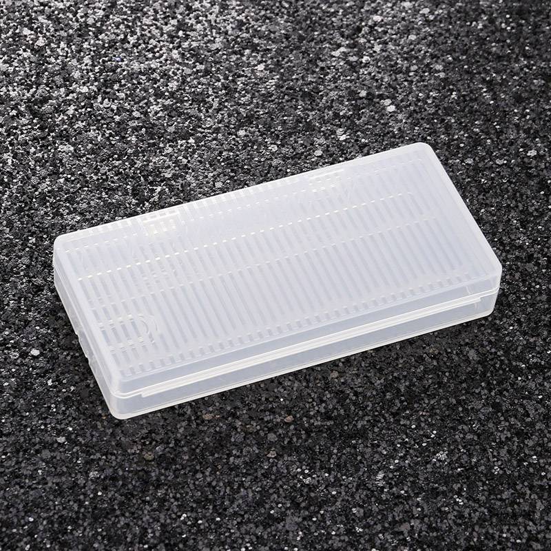 Ein transparentes, rechteckiges Plastikgehäuse liegt auf einer schwarzen, körnigen Oberfläche.