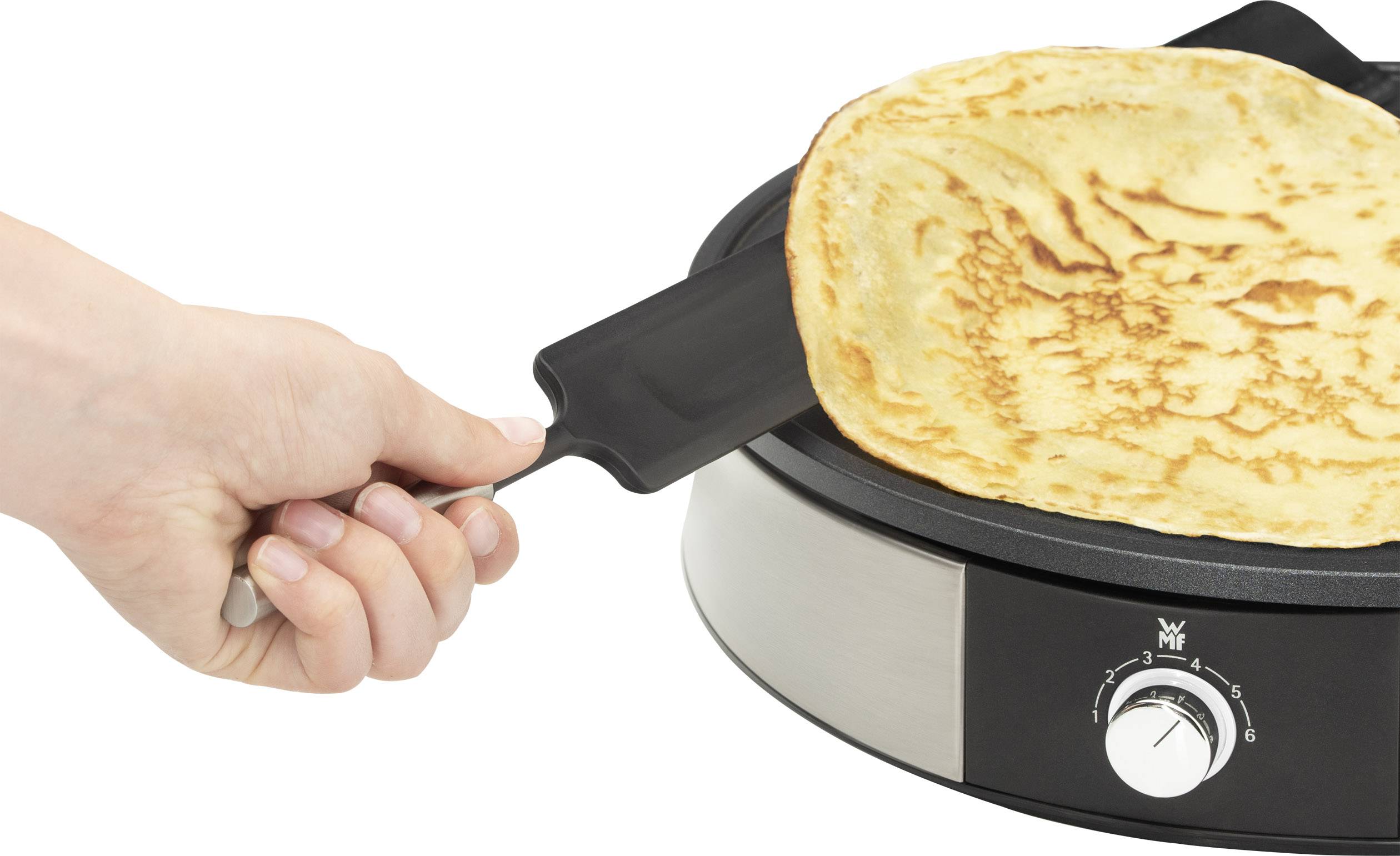 Eine Hand wendet einen goldbraunen Pfannkuchen auf einem runden, elektrischen Crepe-Maker mit Temperaturregler.