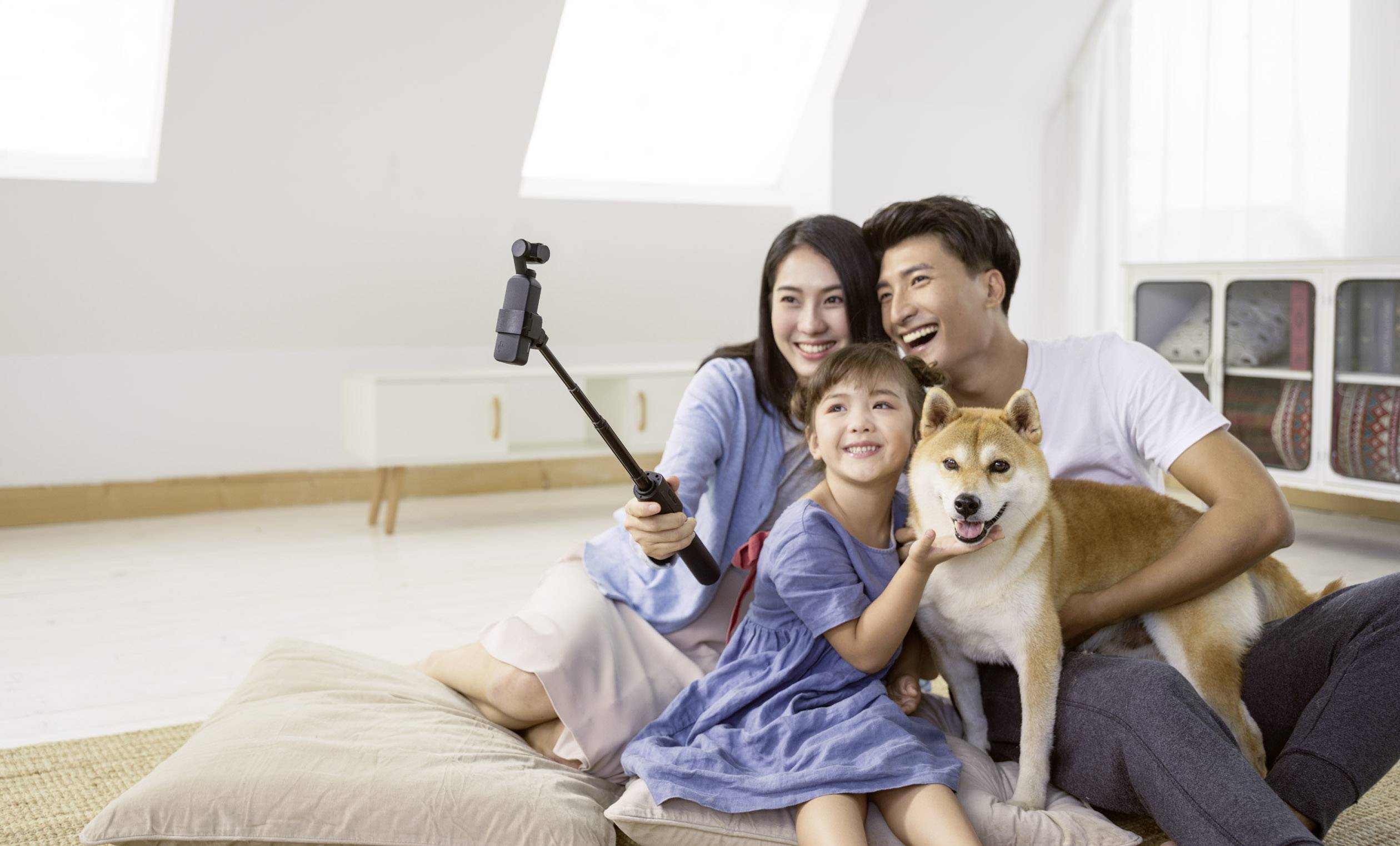 Eine lächelnde Familie sitzt zusammen auf dem Boden und macht ein Selfie. Ein Kind umarmt einen Hund, während Eltern daneben sitzen.