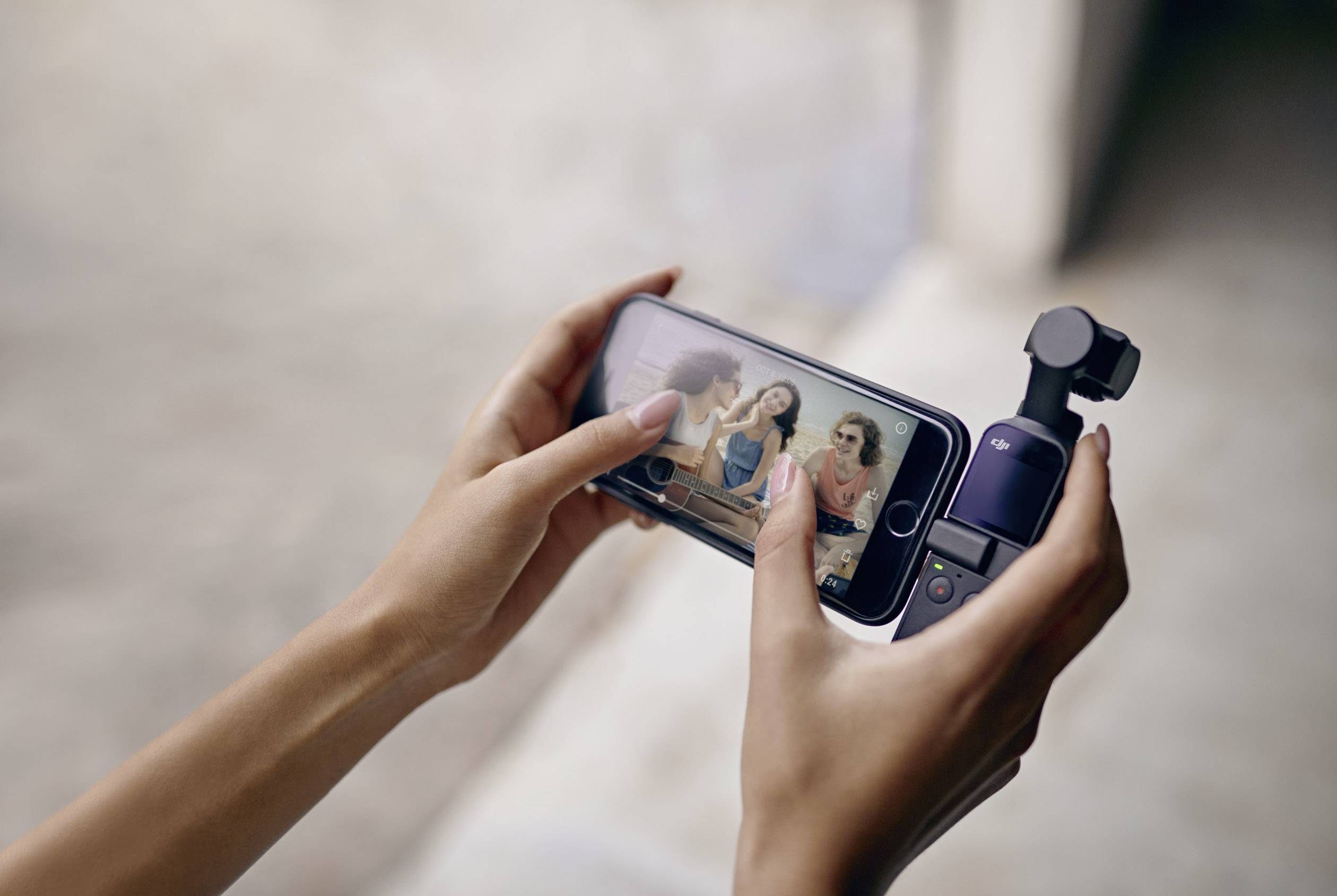 Zwei Hände halten ein Smartphone und eine kleine Kamera. Auf dem Bildschirm des Smartphones ist ein Videoanruf mit drei Personen sichtbar.