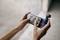 Zwei Hände halten ein Smartphone und eine kleine Kamera. Auf dem Bildschirm des Smartphones ist ein Videoanruf mit drei Personen sichtbar.