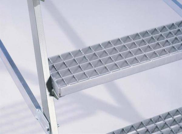 Eine Nahaufnahme von silbernen Metallstufen mit einem Gittermuster, Teil einer Leiter oder Treppe in einem industriellen Umfeld.
