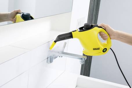 Szene in einem Bad. Eine Hand hält einen Dampfreiniger über eine Edelstahlarmatur. Der Dampfreiniger stammt von der Firma Kärcher, hat ein gelbes Gehäuse und einen gebogenen Düsenaufsatz. Ein Kabel führt vom Gerät weg.