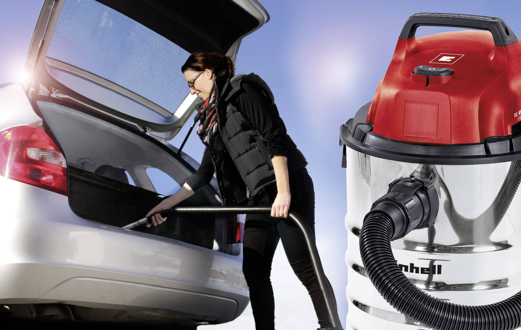 Eine Person saugt den Kofferraum eines Autos mit einem Industriesauger. Der Staubsauger hat einen roten Deckel und einen flexiblen Schlauch.