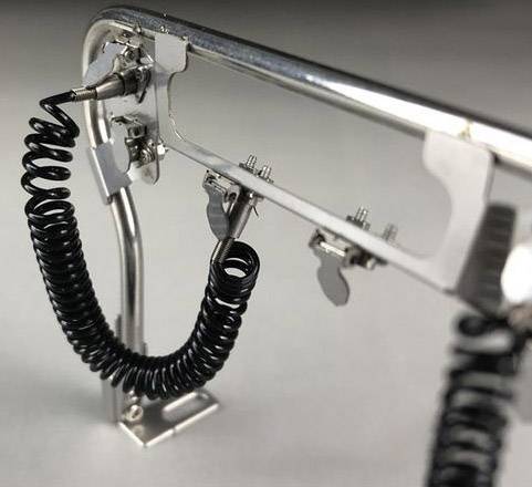 Metallkonstruktion mit einem gewundenen Kabel und Befestigungen, auf einer flachen Oberfläche stehend, vor neutralem Hintergrund.
