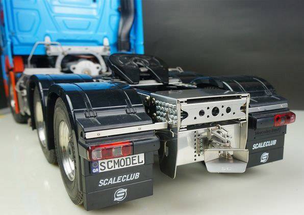 Ein Modell-LKW-Anhänger mit detaillierten Teilen und blauer Kabine ist auf einer ebenen Oberfläche abgebildet.