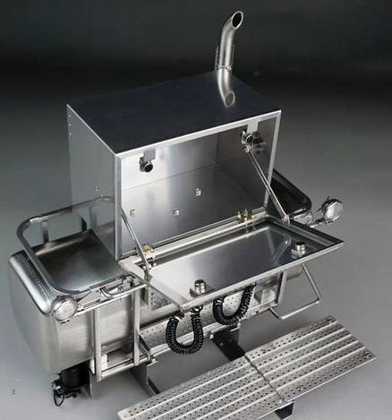 Ein Metallgrill aus Edelstahl mit zwei Rädern, einem Rohr oben und einer aufklappbaren Abdeckung, steht in einem Raum.