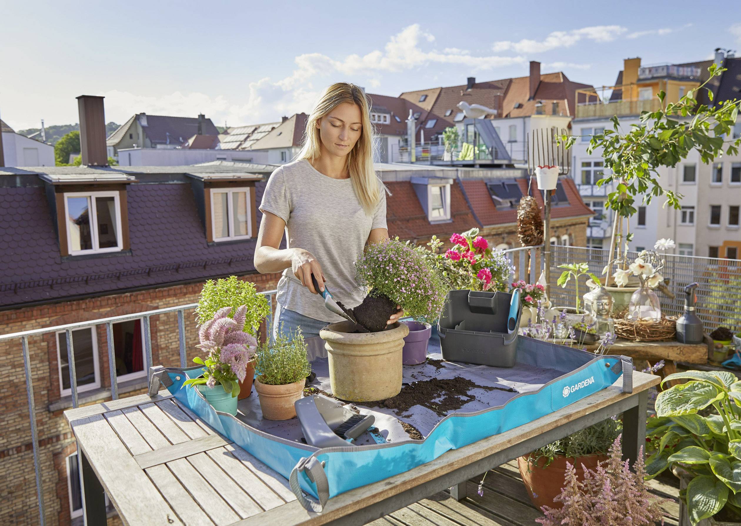Eine Frau pflanzt Blumen auf einem Stadtbalkon. Sie setzt eine Pflanze in einen Topf auf einem Tisch mit gärtnerischen Werkzeugen ein.