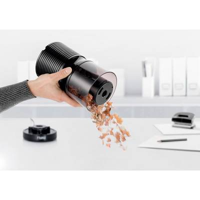 Eine Hand leert einen Staubsaugerbehälter mit Schmutz und Staub in einen Mülleimer. Bürogegenstände sind im Hintergrund sichtbar.