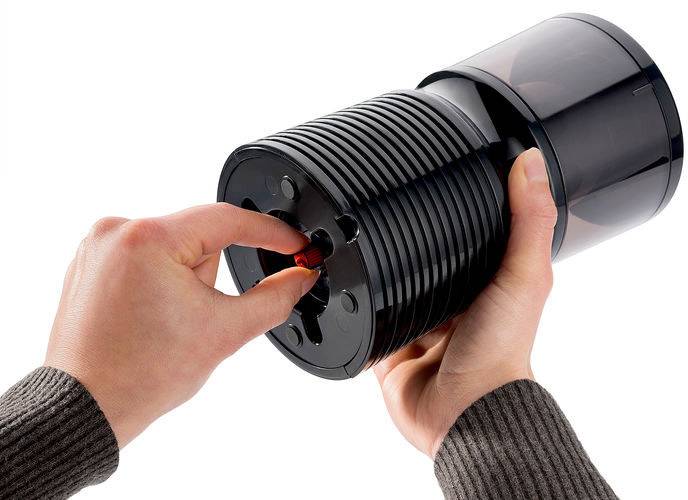 Eine Person dreht eine rote Scheibe an einem zylindrischen Gerät. Hände umfassen den Zylinder.