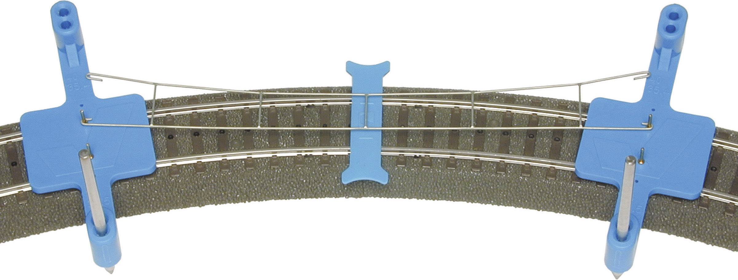 Eine gebogene Modellbahnstrecke mit zwei blauen Halterungen darauf, die einen dünnen Draht führen.