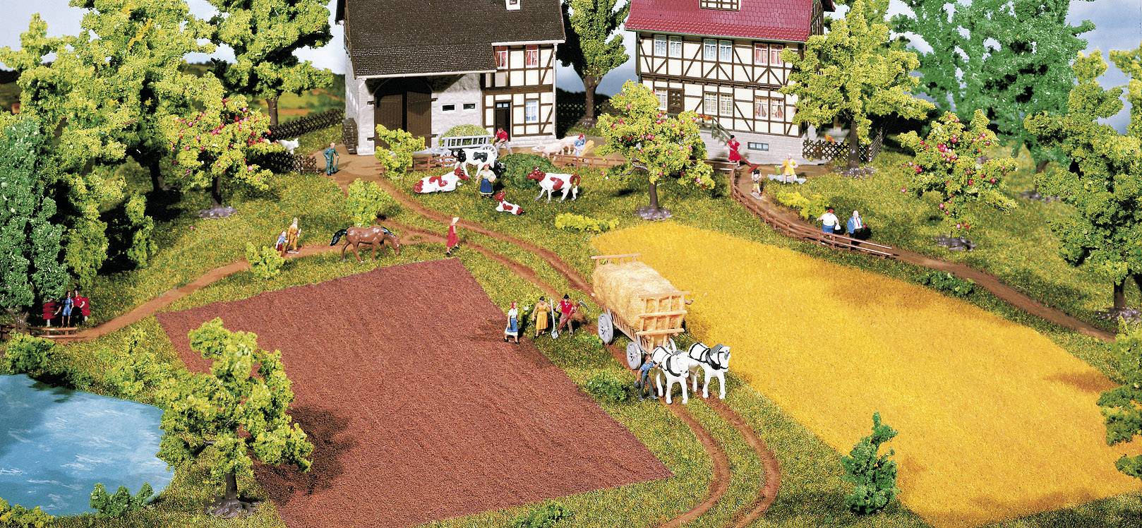 Eine ländliche Szene zeigt einen Bauernhof mit zwei Fachwerkhäusern, Feldern, Kühen und einem Pferdekarren. Menschen arbeiten auf dem Feld.