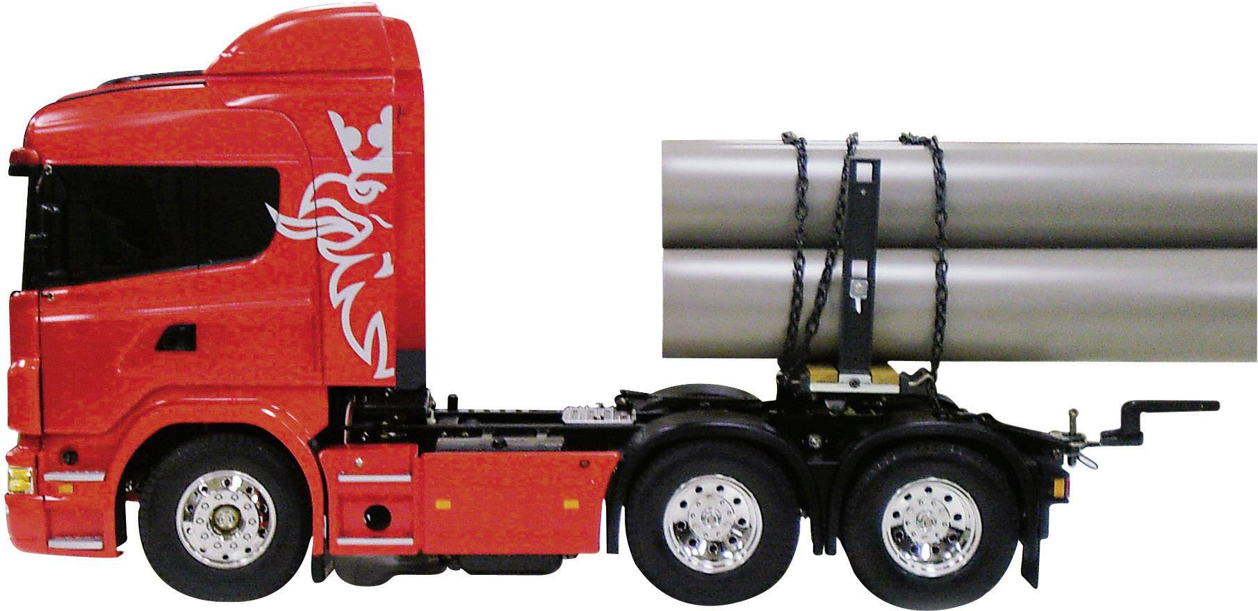 Roter Lastwagen mit schwarzen Felgen und zwei langen, braunen Röhren, gesichert mit Ketten auf der Ladefläche.