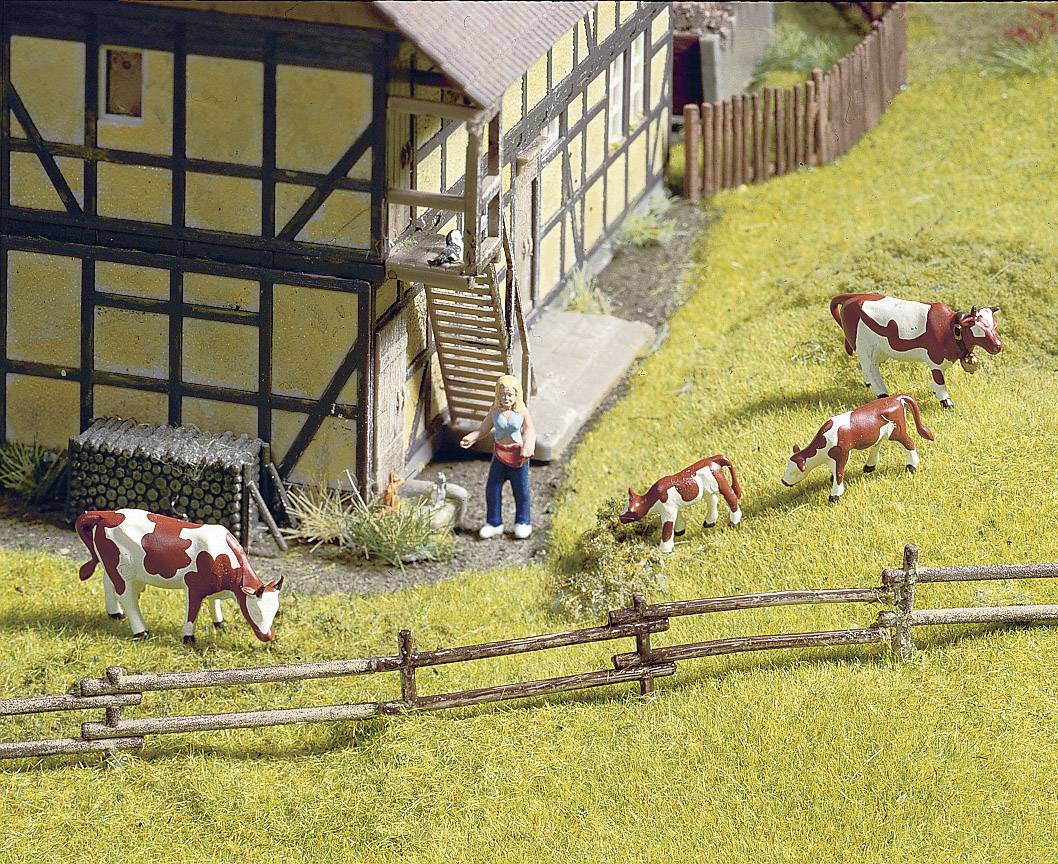 Eine Miniaturszene zeigt ein Fachwerkhaus mit einer Person, die einen Eimer hält, und mehrere Kühe auf einer Wiese neben einem Holzzaun.